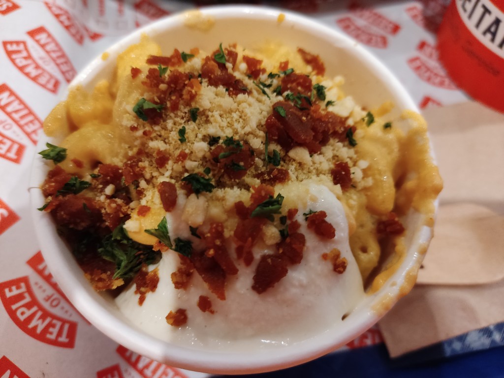 A pot filled to the brim with mac and cheese hopped with bacon crumbles and sauce
