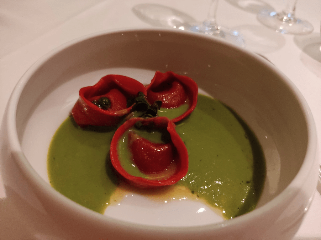 A white bowl containing three bright red tortellini with a green sauce