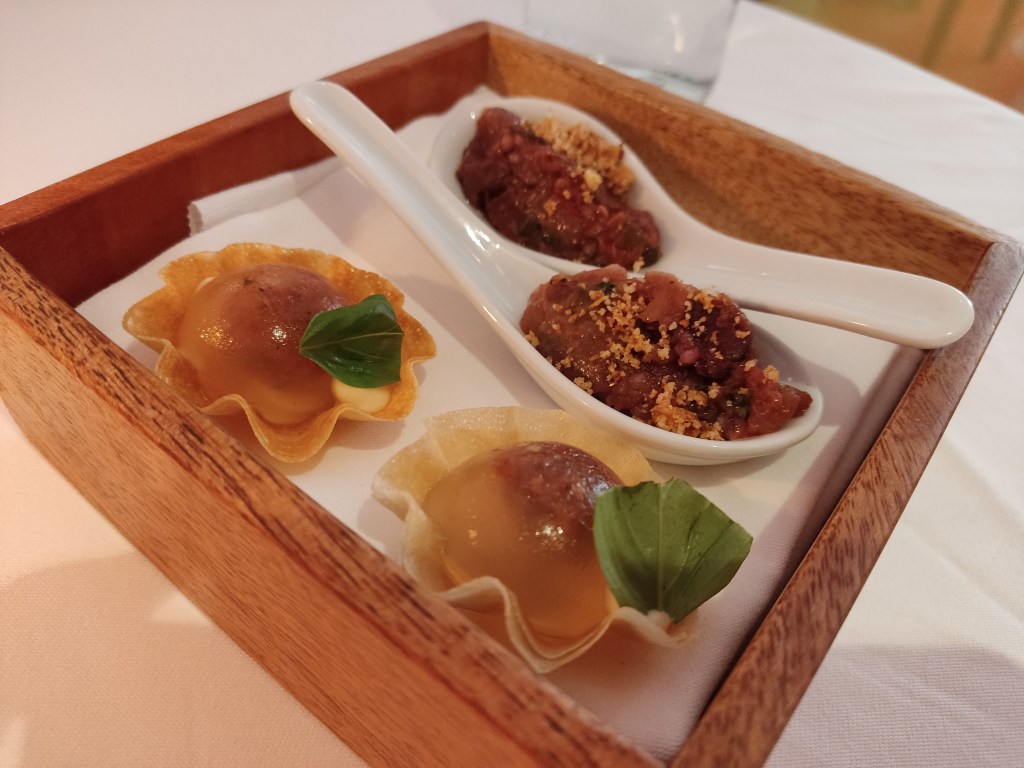 Two small tarts in crisp, thin shells with a gel dome in the centre. Two spoons with a rich aubergine coloured concoction.