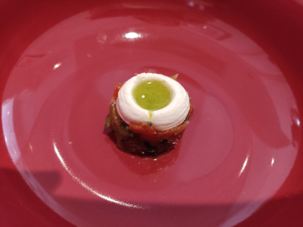 A small cylinder of pico de gallo, topped with a creamy feta with a pool of green oil in a well in the centre.