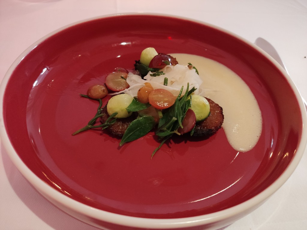 A red plate with artfully arranged vegetables and a creamy beurre blanc on the side