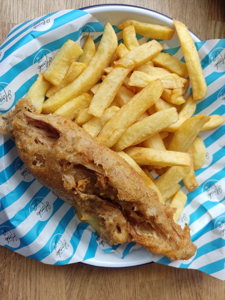 A crispy battered banana blossom fish served with a generous helping of chips on blue and white stripy paper