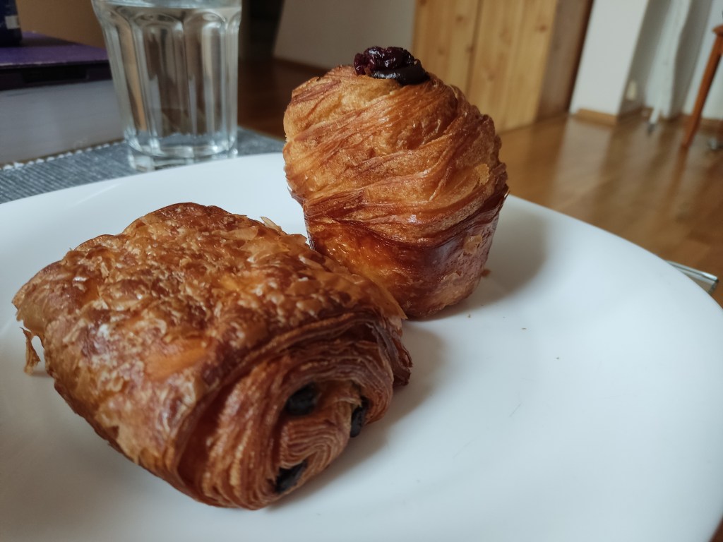 Two pastries on a plate. One is a pain au chocolat and the other is a cross between a croissant and a muffin