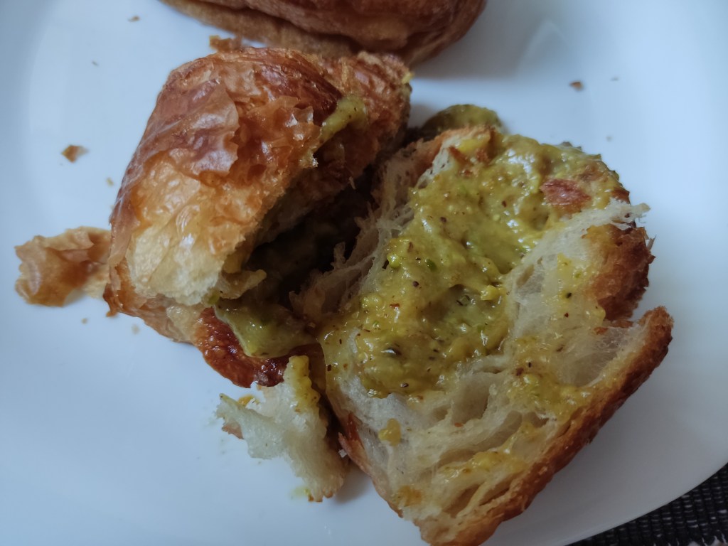 A croissant muffin cut in half, filled with pistachio cream