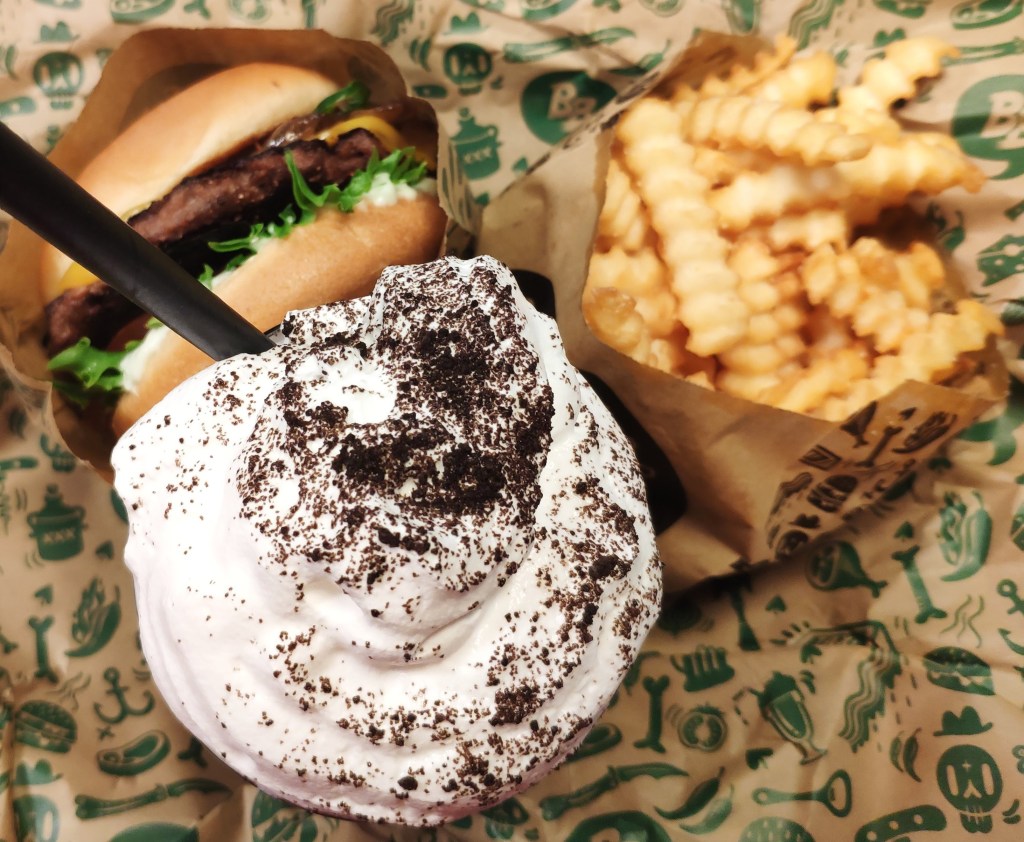 A burger, a bag of crinkle cut fries and a huge creamy milkshake