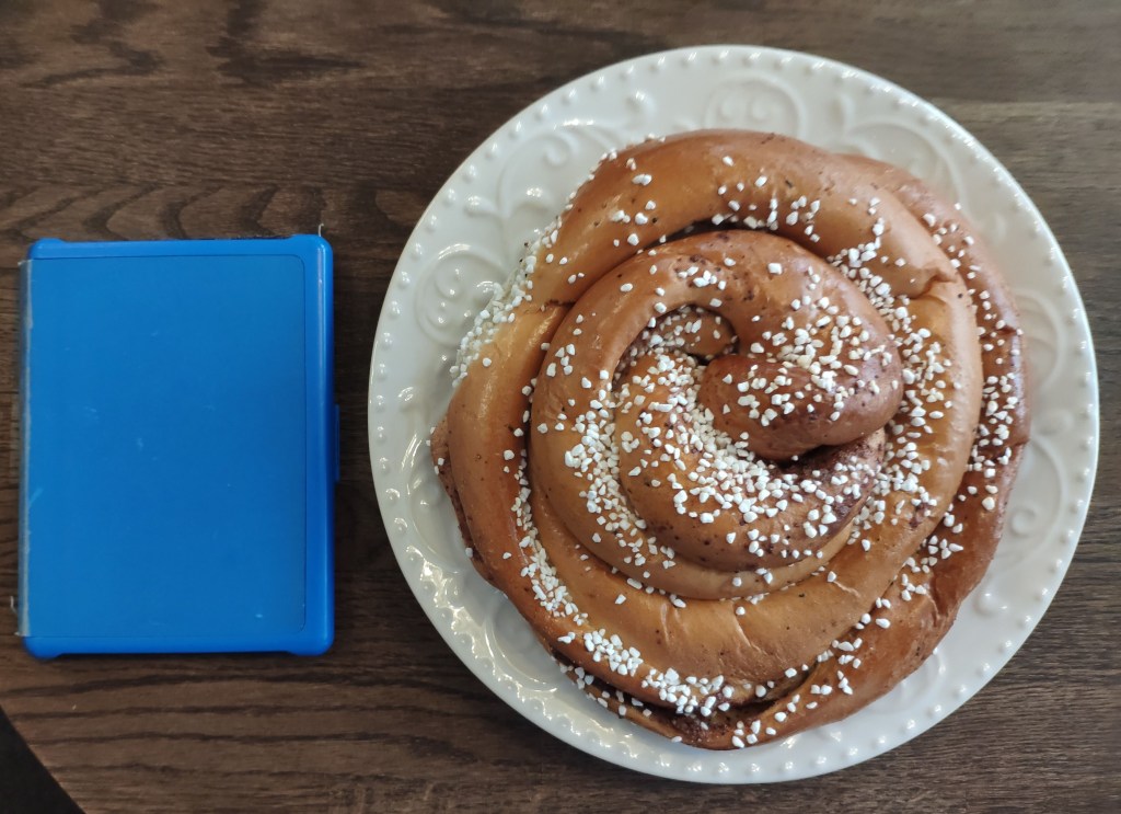 A cinnamon bun next to a Kindle, to show the scale. The bun is quite a bit larger than the Kindle.