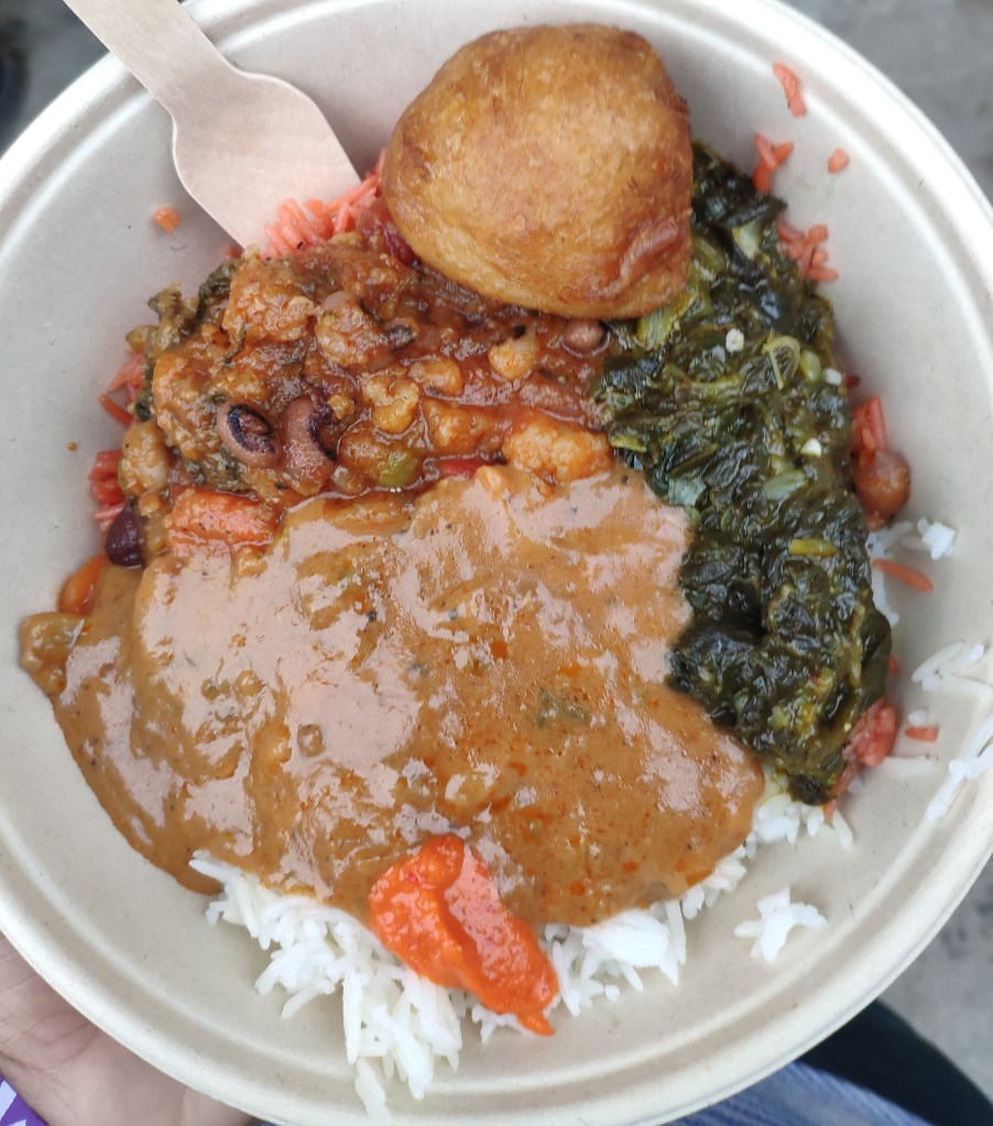 A big bowl with rice at the bottom topped with a variety of different saucy vegetable dishes