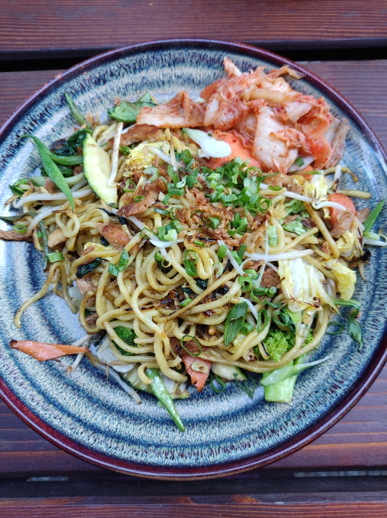 A plate of noodles, fresh herbs, vegetables and a big helping of orange kimchi