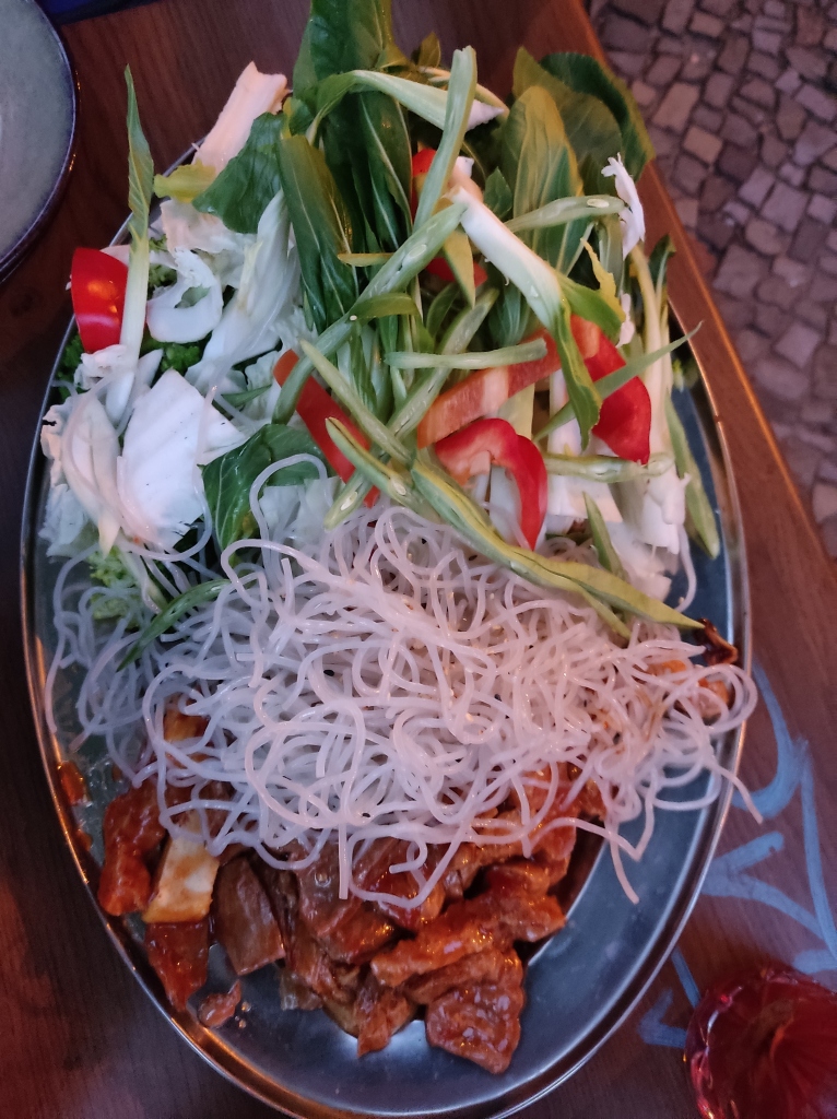 A large metal plate with chunks of marinated soy, white noodles, and uncooked vegetables and herbs