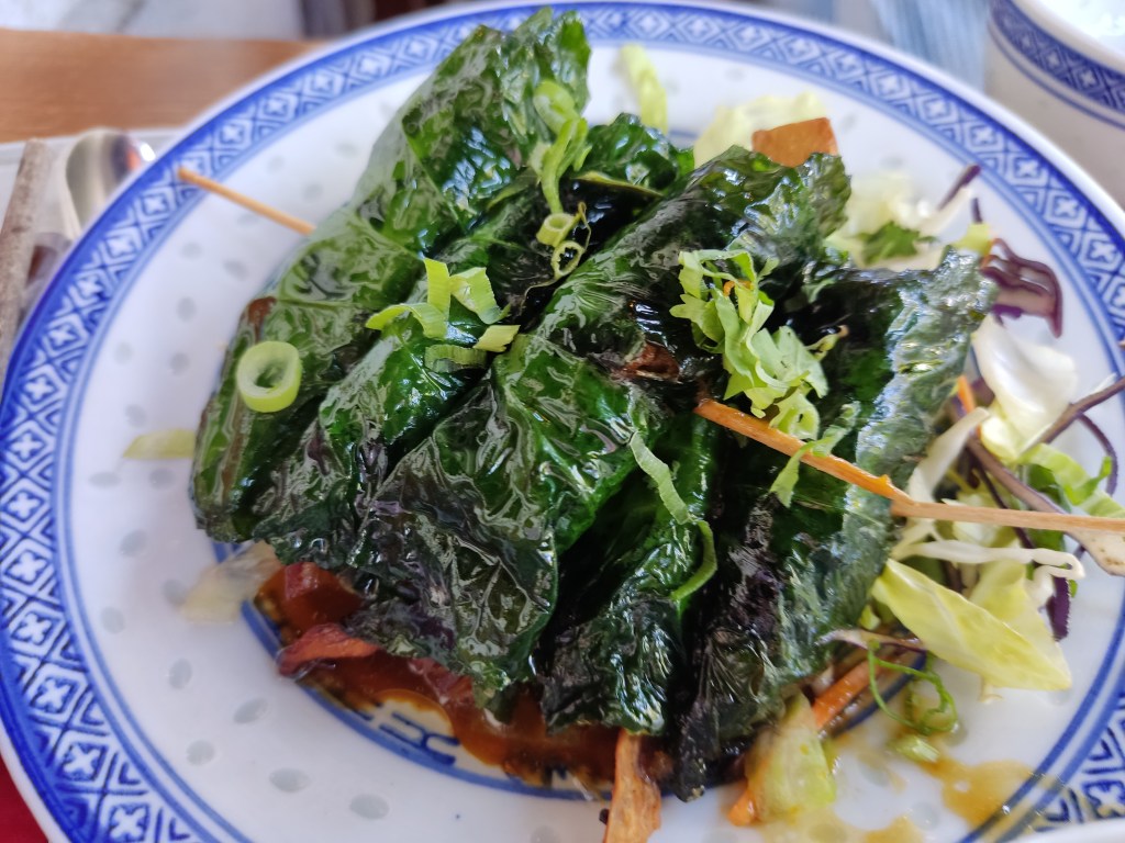 Two skewers each holding three stuffed leaves, on a bed of fresh salad