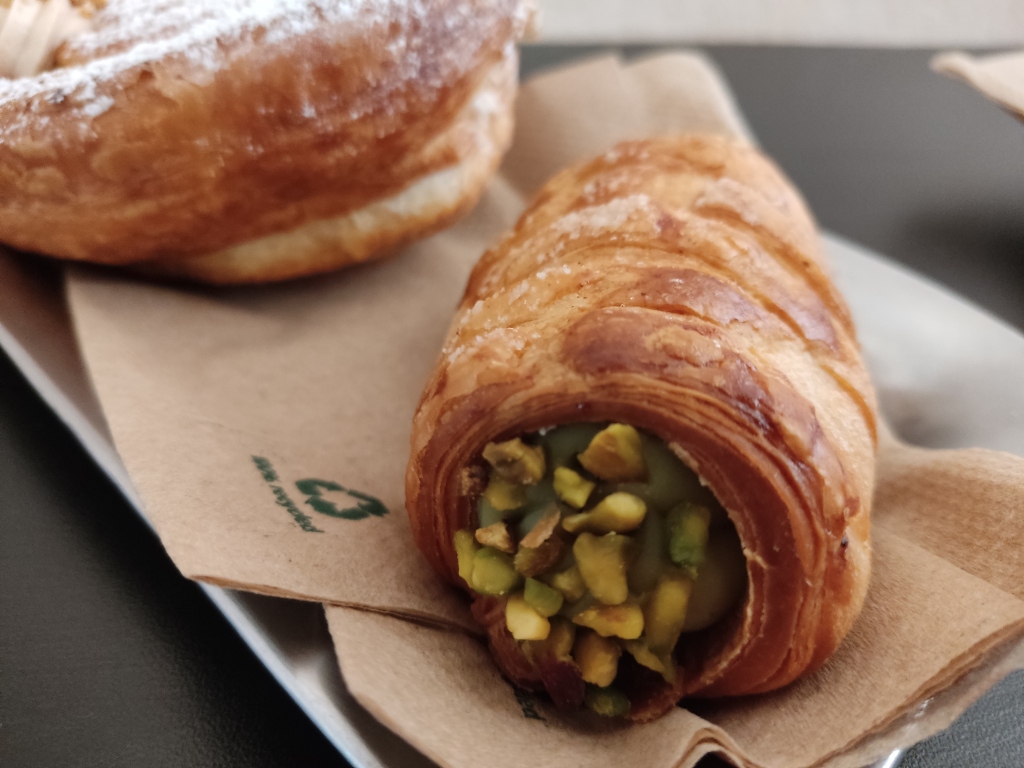A crispy pastry tube filled with light green pistachio cream and adorned with some pistachio chunks