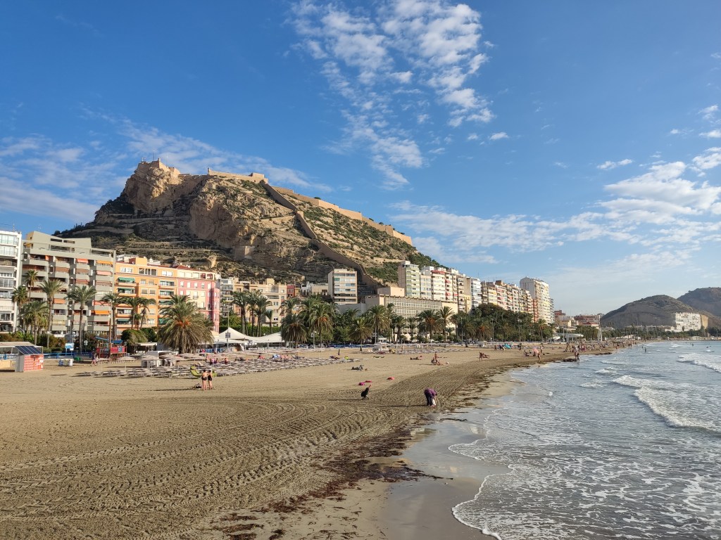 The sea and beach of Alicante, with the castle sitting on top of a hill in the background