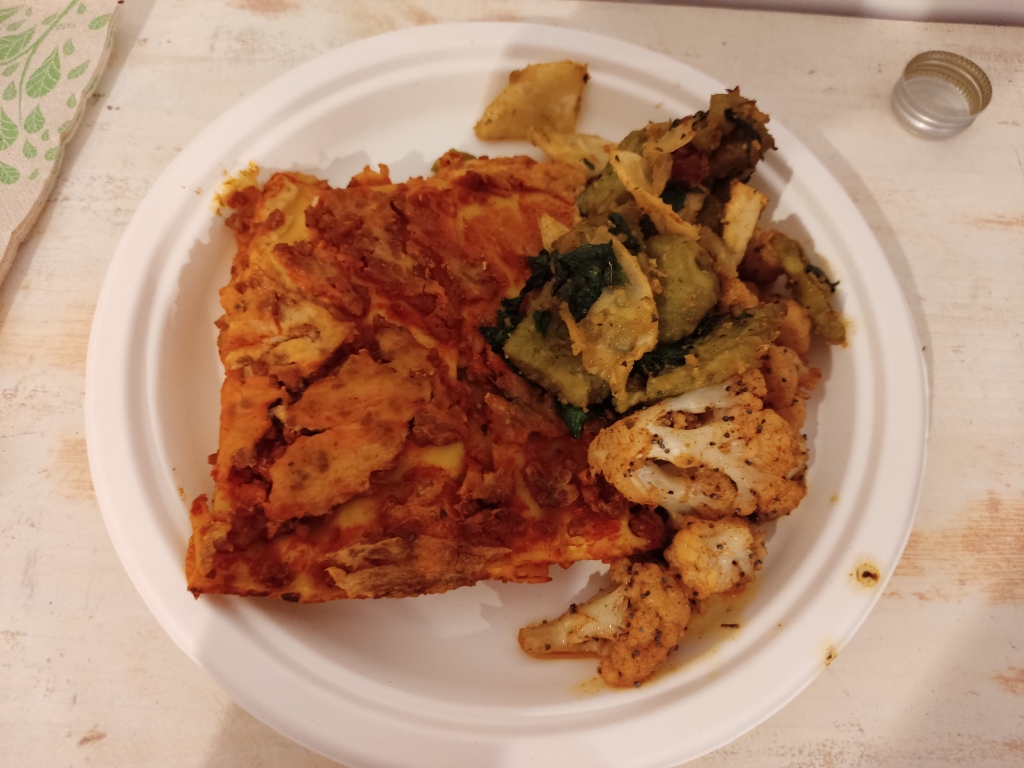 A slice of lasagna with notable ragu and bechamel colours, alongside some vegetable side dishes