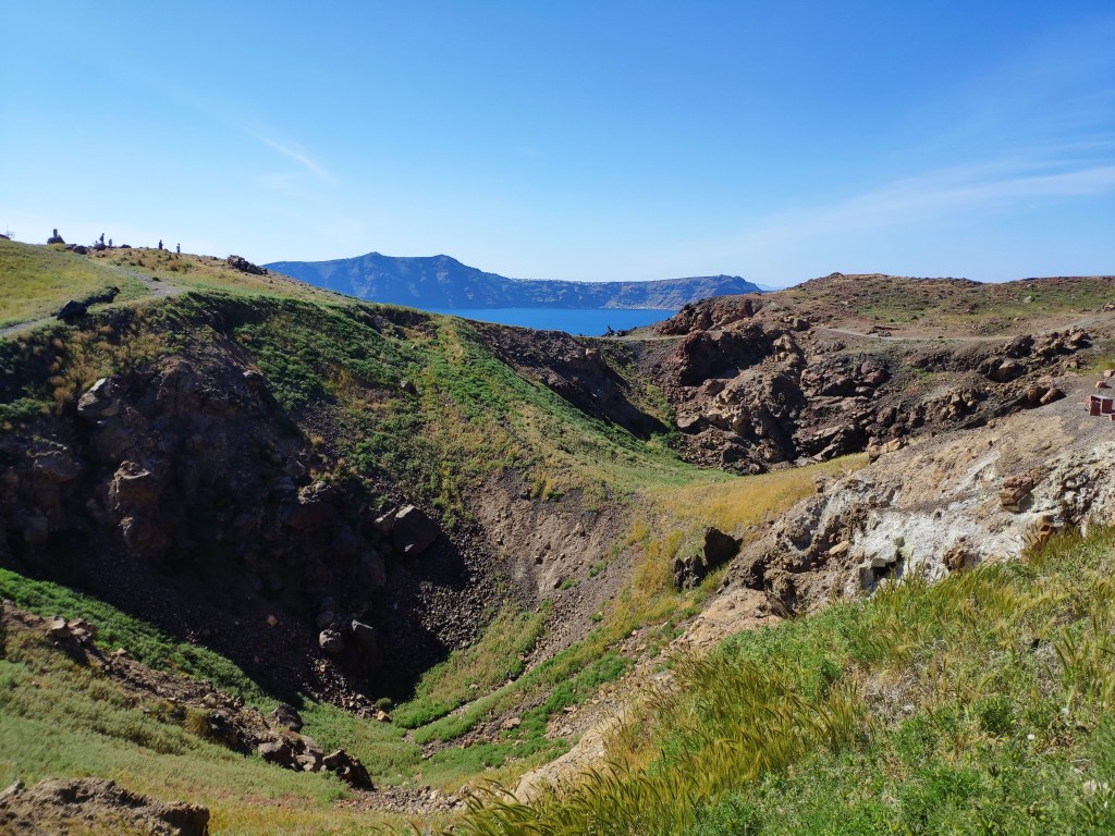 The crater of the volcano, with blue sea, sky, and Santorini in the background