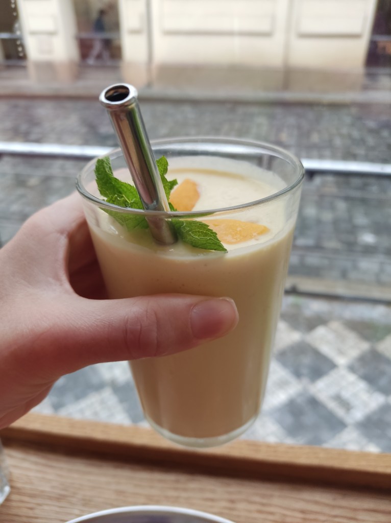A glass filled with creamy yellow mango lassi, topped with fresh mint leaves and served with a metal straw