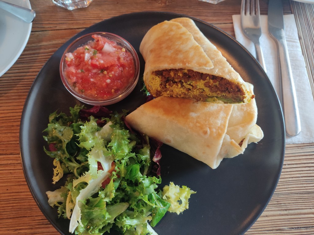 A breakfast burrito served with a pot of salsa and a side salad