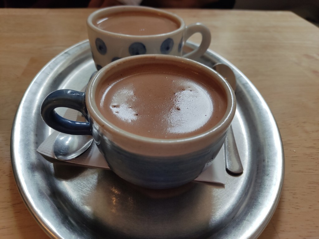 Two small cups of thick hot chocolate on a silver tray on a table