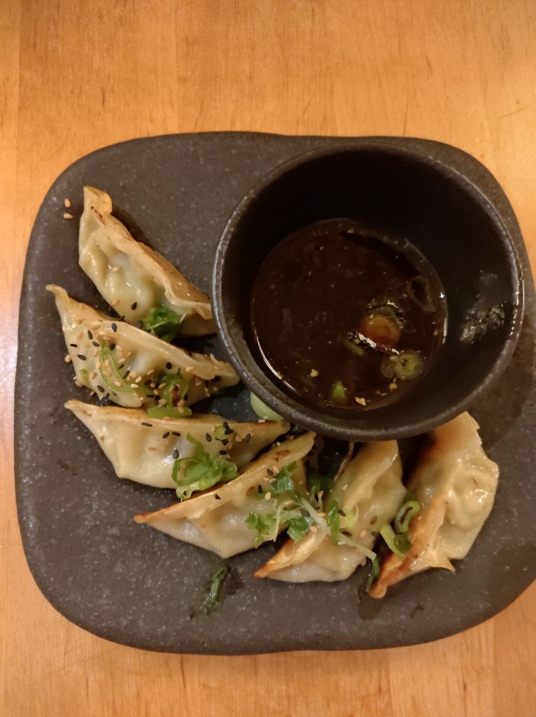 Six fried gyoza with a bowl of dipping sauce