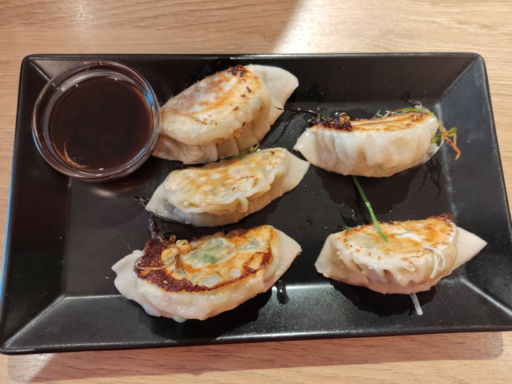 Five fried gyoza with a small pot o dark dipping sauce