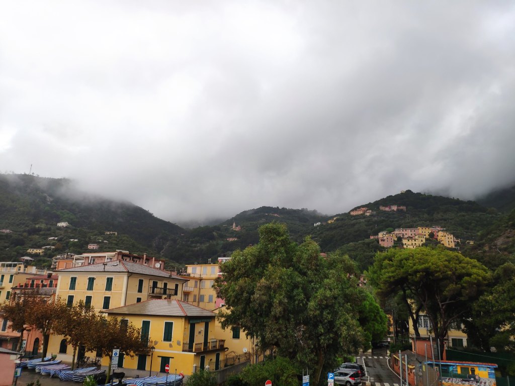 The town of Bonassola with yellow buildings in the foreground and dark green hills rising in the background, their peaks lost in the dark clouds