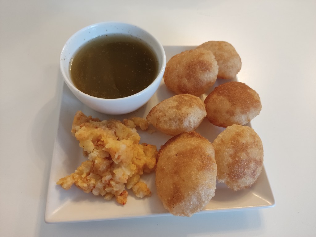 A plate with six puri pieces, crispy hollow balls, a little mound of potato mix, and a bowl of greenish sauce