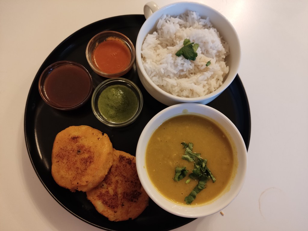 Two potato cakes, a pot of rice, a yellow soup, and three dipping sauces
