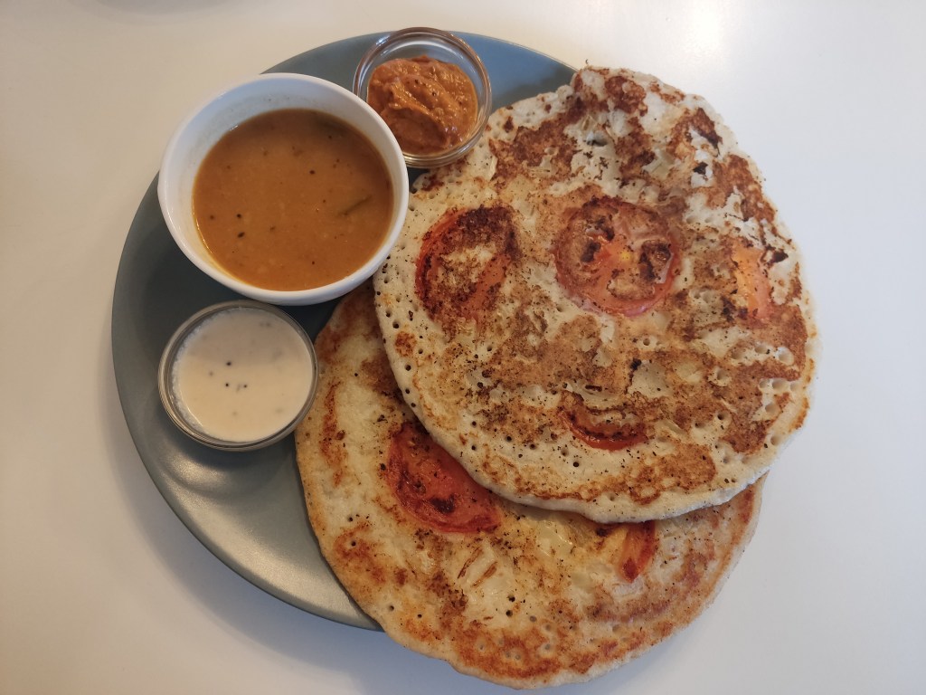 Two pancakes with tomato slices cooked into them, a small pot of soup, and two dipping sauces