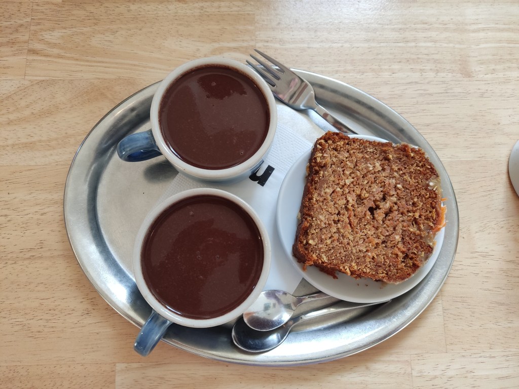 Two cups of thick hot chocolate and a slice of carrot cake