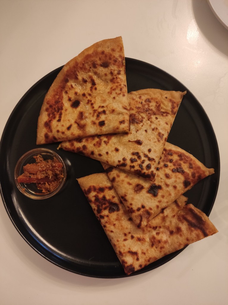 Four quarters of a paratha, looking well fried, with a small pot of chutney.