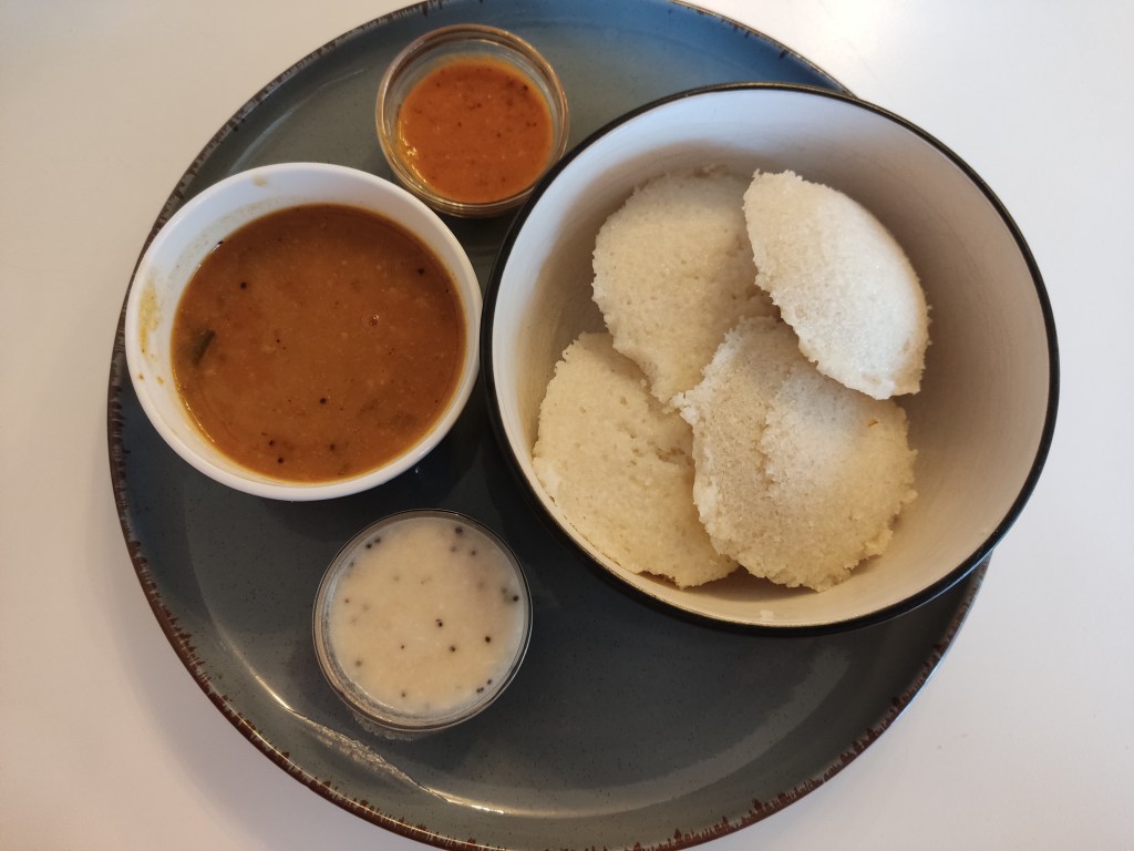 A bowl with flour fluffy white savoury cakes, accompanied by a little pot of soup and two dipping sauces.