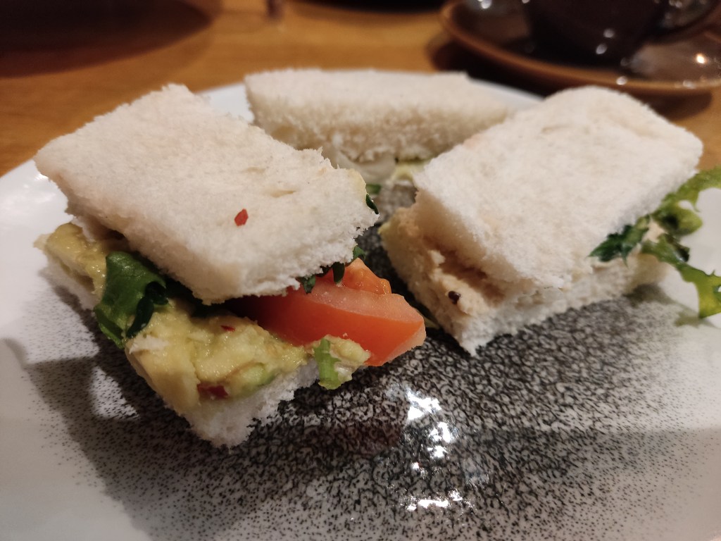 Three finger sandwiches on white bread, one with salad leaves poking out and the other with visible avocado and tomato