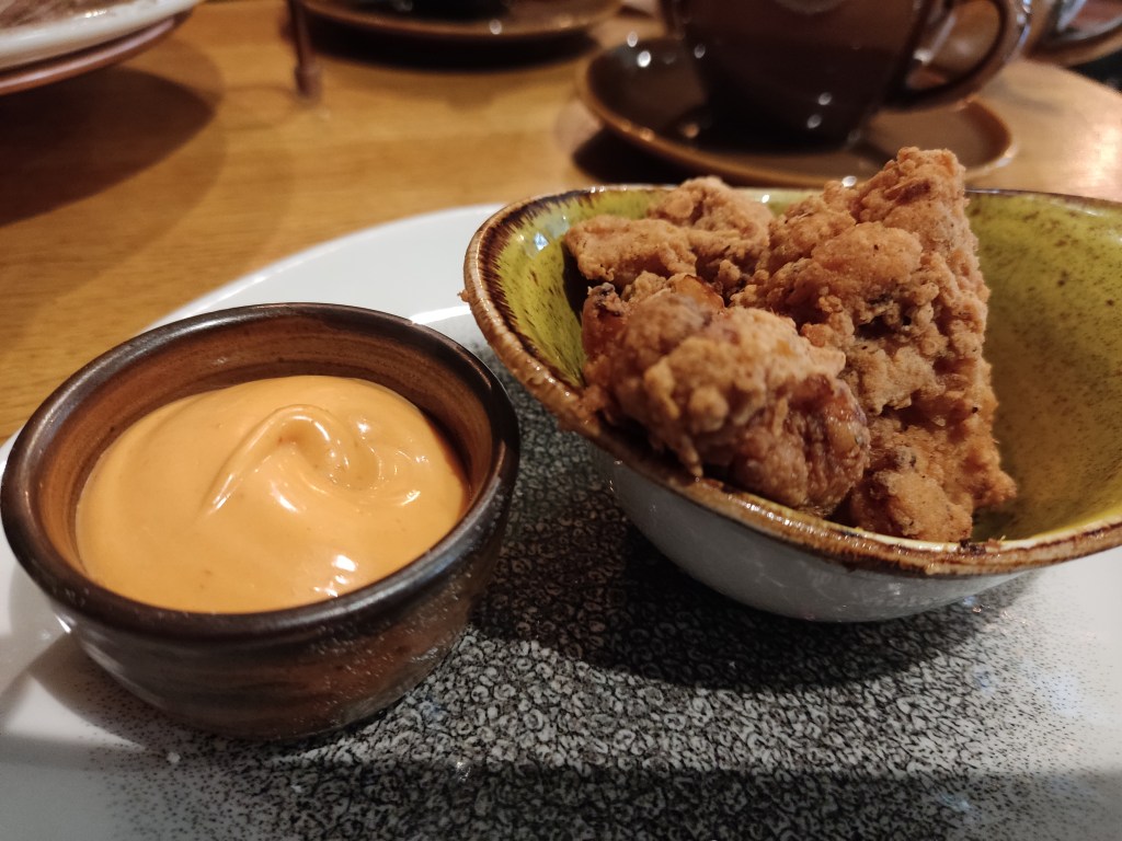 A bowl of cauliflower coated in a crisp looking batter and a small pot of orange dipping sauce