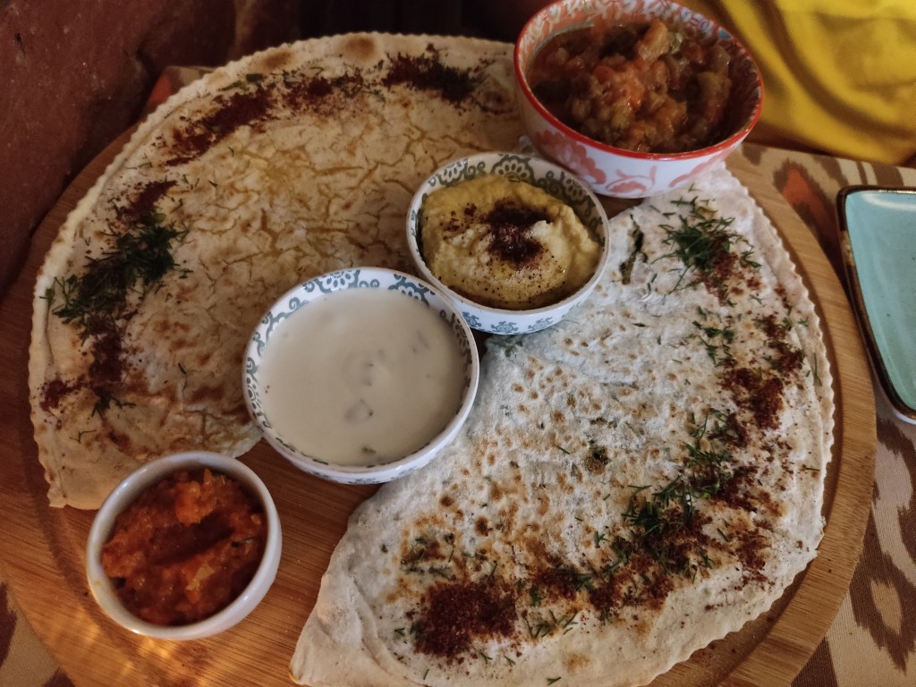 Two large semi circles of filled flatbread, with four small pots of dip in the middle of the dish