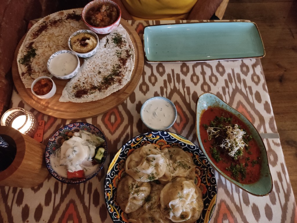 a table with various plates for sharing, including a kofta, dumplings, salad with a yoghurt dressing, and flatbreads with dips