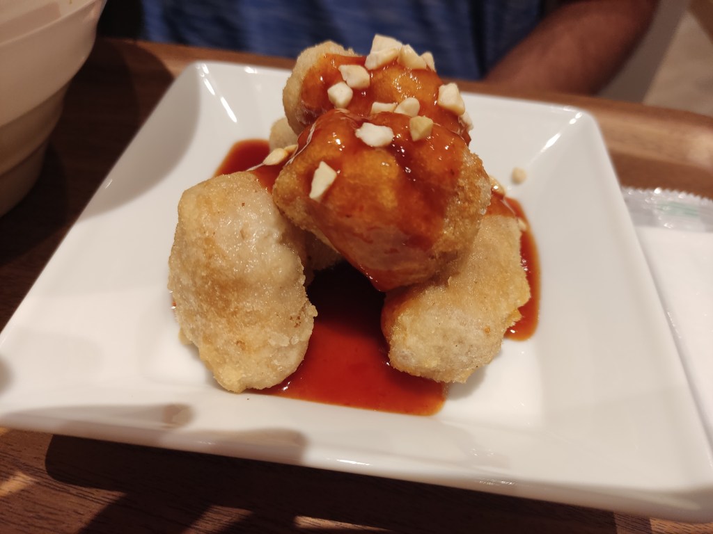 A plate with several pieces of battered vegan chicken in a thin bright red sauce