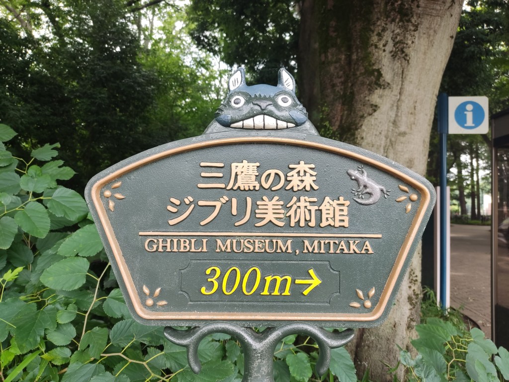 A sign pointing to the Ghibli museum with fun critters on it