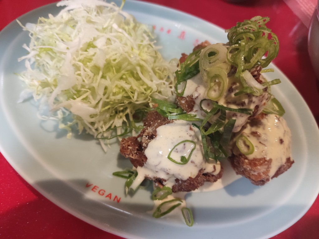A plate containing shredded cabbage dressed with mayo, and some large deep fried chicken chunks dressed with mayo and spring onions