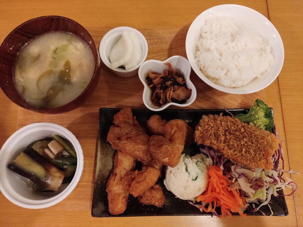 A meal set consisting of little bowls of pickles, miso soup, and rice, alongside a plate containing mock meat pieces and salad