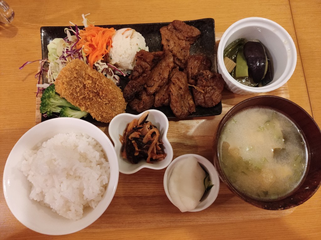 A meal set consisting of little bowls of pickles, miso soup, and rice, alongside a plate containing mock meat pieces and salad