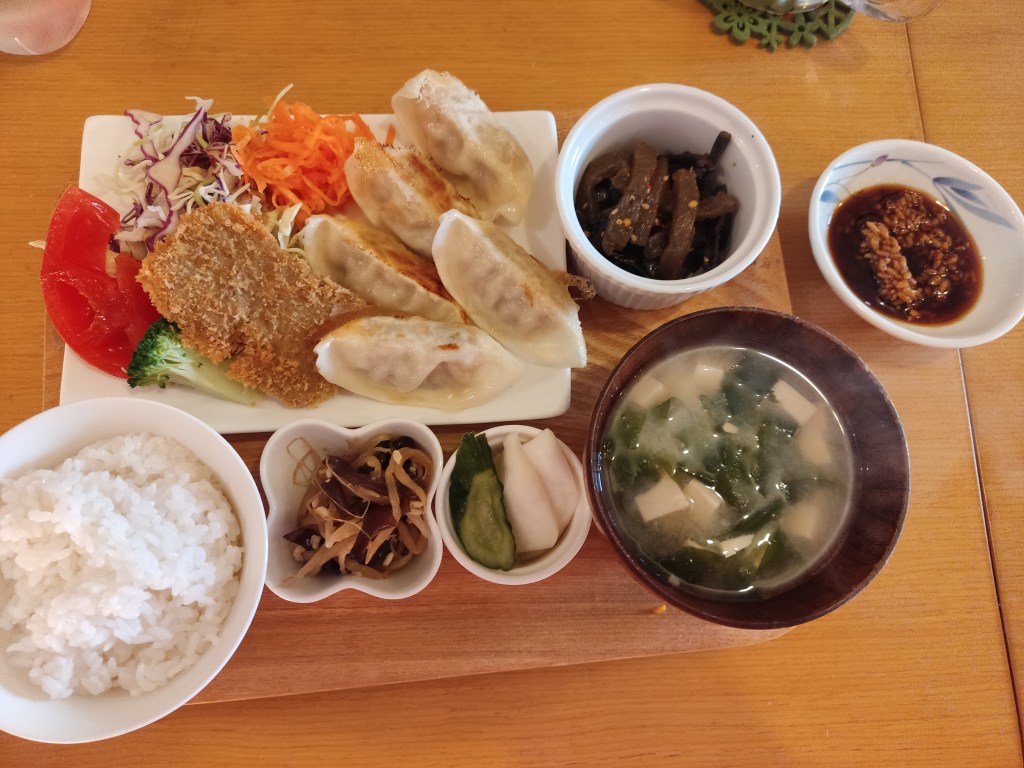 A meal set consisting of little bowls of pickles, miso soup, and rice, alongside a plate containing gyoza and salad