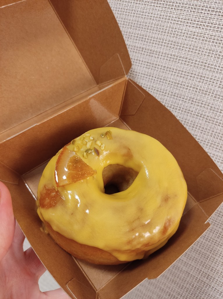 A doughnut covered in a sticky looking yellow glaze with a little candied lemon piece on top.