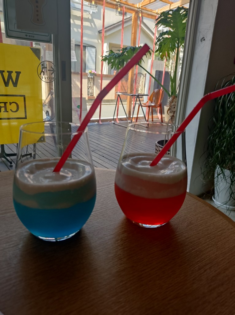 Two glasses, one with a bright blue soda and the other with a bright red soda. Both are topped with a thick creamy layer.