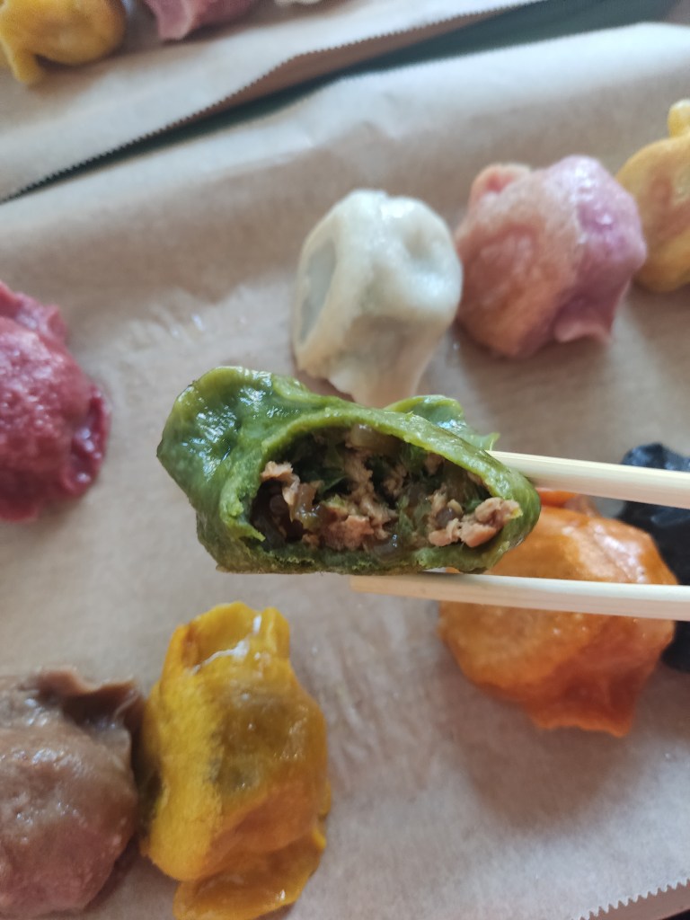 An open gyoza being held up with chopsticks. It has a green wrapper. Inside there is vegan mince and green herbs.