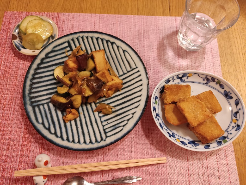 A small dish of pickled cucumber, a portion of fried mushrooms and tofu, a plate with five big pieces of battered and fried tofu.