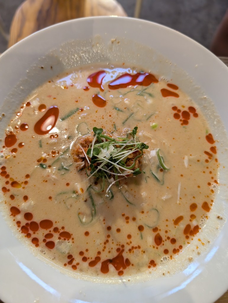 A bowl of ramen with a thick creamy broth split with a red oil, topped with some mock meat and microgreens in the centre of the bowl