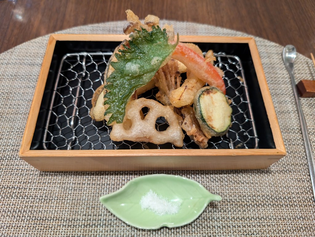 An assortment of tempura vegetables, including a shiso leaf, lotus root, enoki mushrooms, red pepper, and courgette