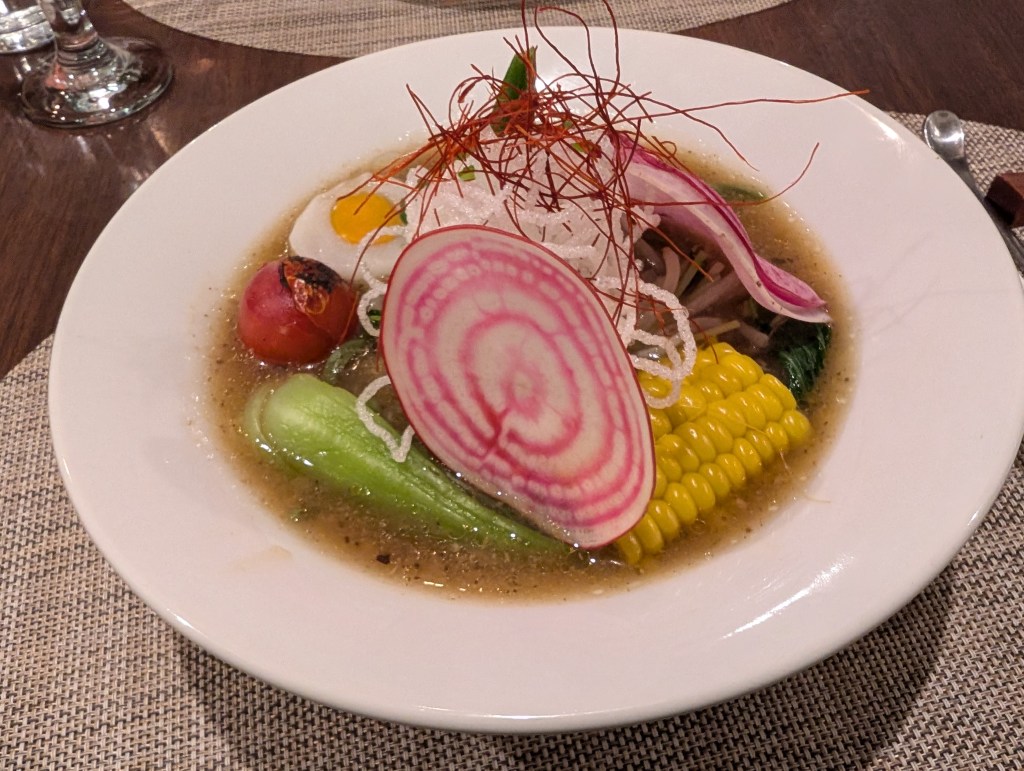 A bowl of ramen with lots of vegetables and a vegan egg, topped with fried noodles and chilli threads