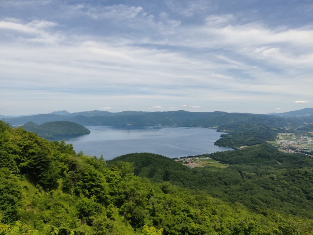 A view from the top of a mountain looking down over green hills and a big lake