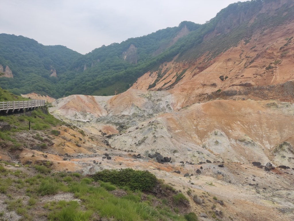 Yellow and grey rocky slopes with green hills in the background and a walkway on the left