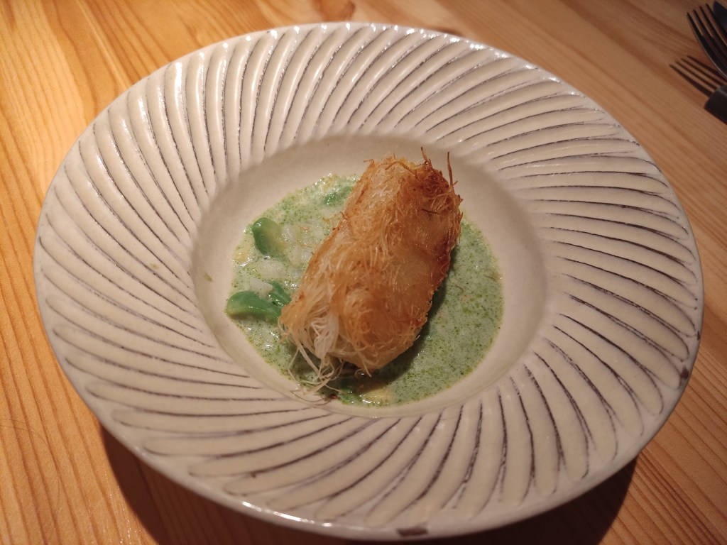 A large nest of crispy threads sitting on a green creamy risotto.